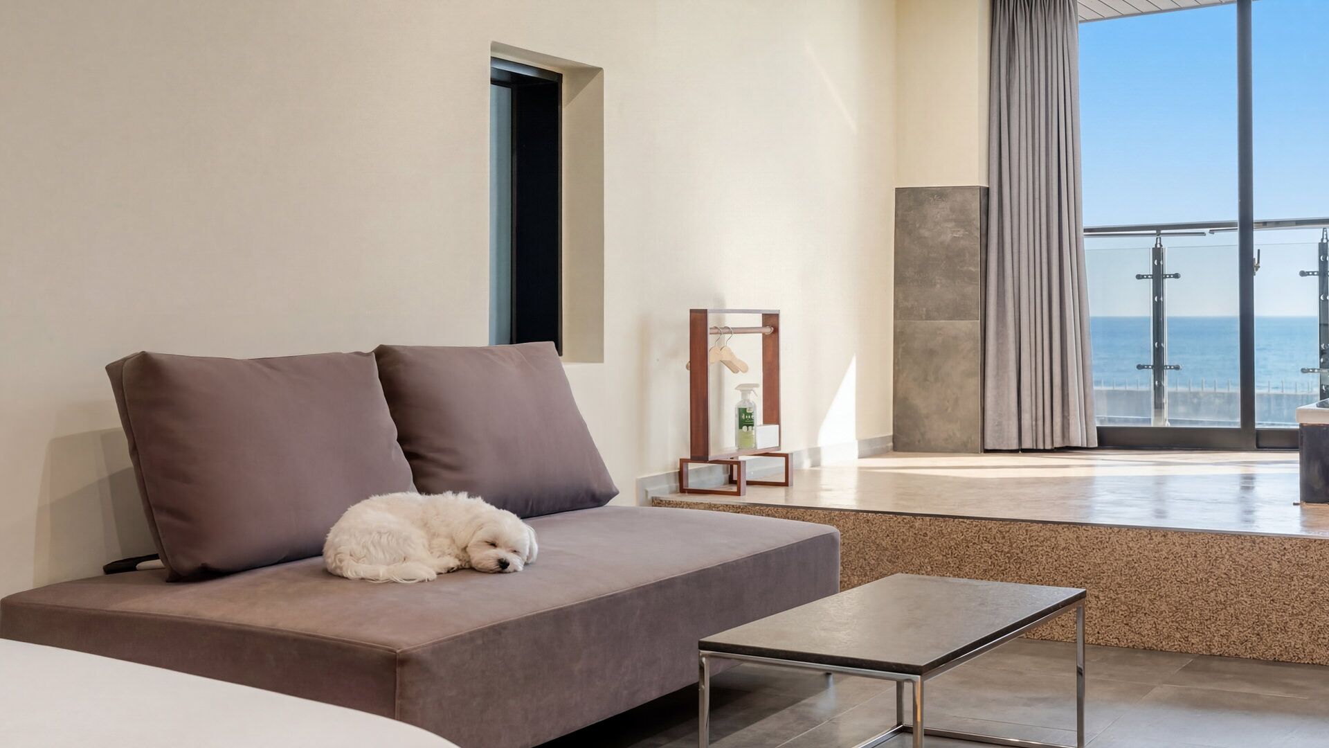 A modern hotel room with a sofa, a small table, and a view of the sea.