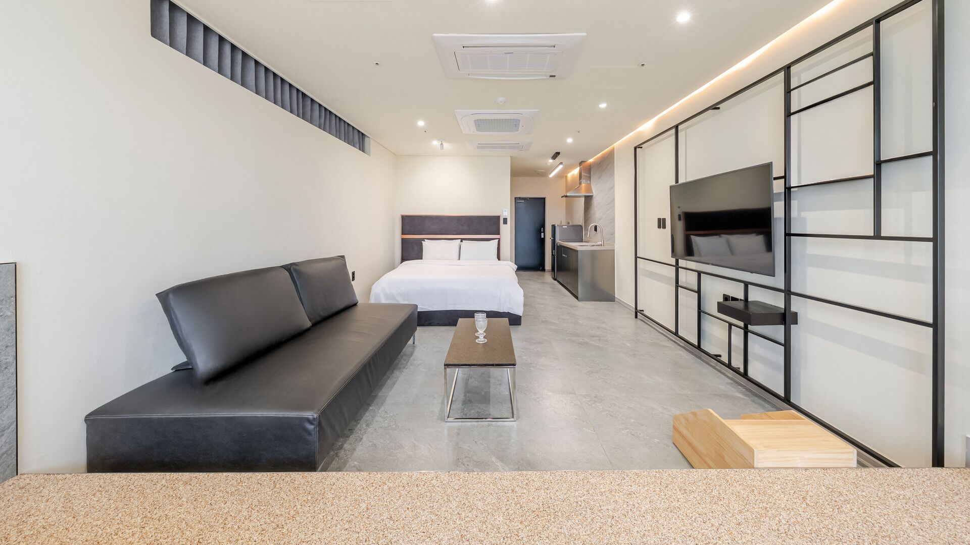 A modern hotel room with a sofa, a bed, a TV, and a kitchenette.