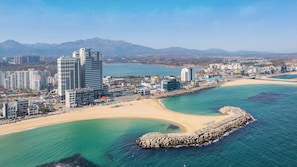 A coastal cityscape with high-rise buildings, a sandy beach, and a rocky breakwater. - Sokcho W&jiseda Spa Poolvilla (Sokcho)