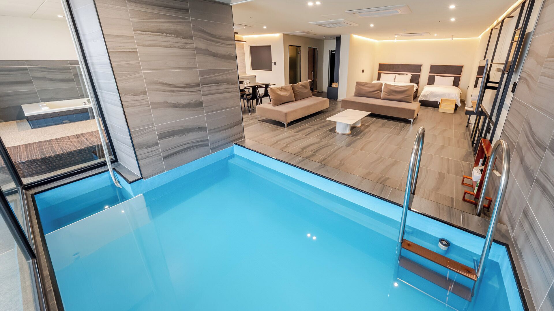 A modern hotel room with a pool, a sofa, a dining area, and a bedroom.