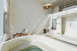 A modern, spacious room with a large bathtub, a wooden table with chairs, a staircase, and a hanging light fixture. - Gangneung Mutenlol (Gangneung)