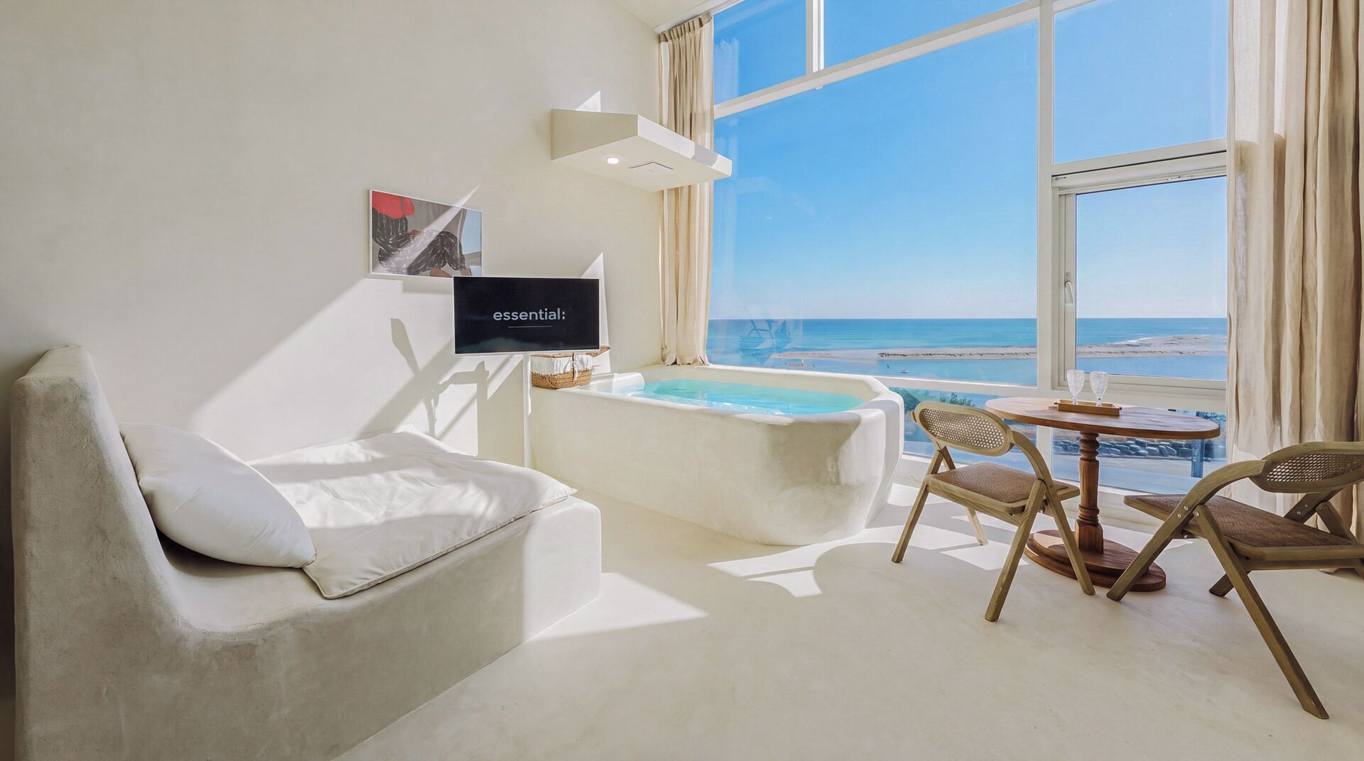 A modern room with a white sofa, a small table with a glass, and a view of the ocean.