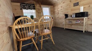 Interior de una cabaña de madera con comedor, cocina equipada con microondas y cama en altillo.