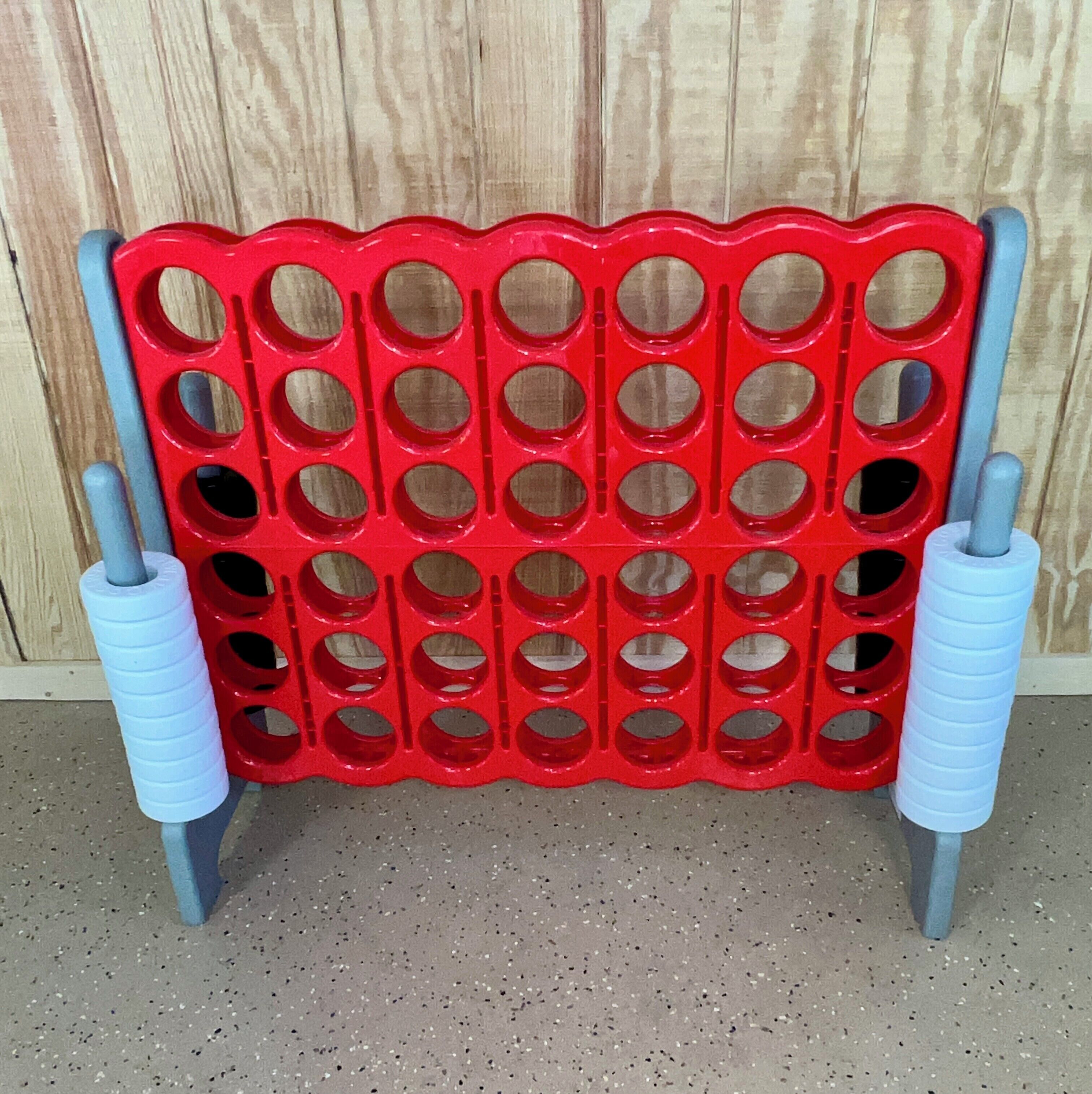 A red plastic board with multiple circular cutouts, supported by two blue cylindrical stands.
