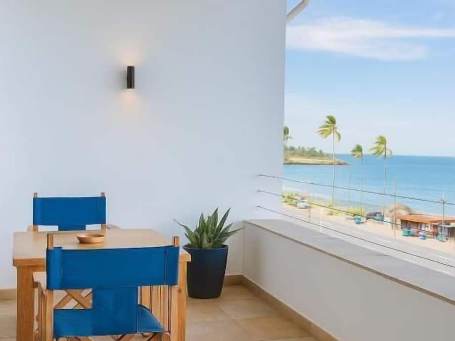Un balcón con vista a la playa, una mesa con sillas y una planta en maceta.