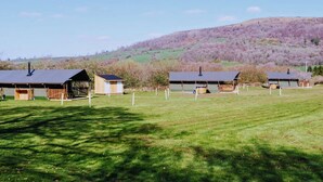 A row of simple, single-story buildings with flat roofs, likely barns or storage sheds, in a grassy field with a hilly backdrop.