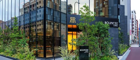 A modern building with a glass facade, a sign for 'BUNCEE by RIHGA', and a landscaped area with plants.