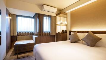 A hotel room with a bed, a seating area, a desk, and a mirror.