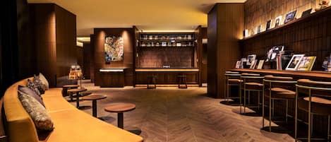 A modern lounge area with a sofa, round tables, a bar with stools, and a bookshelf.