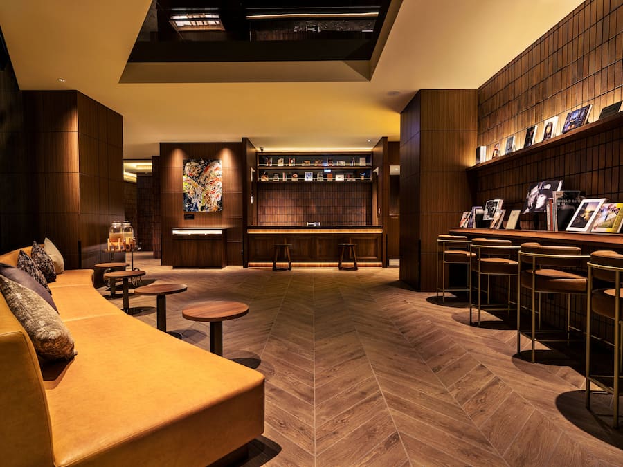 A modern lounge area with a sofa, round tables, a bar with stools, and a bookshelf.