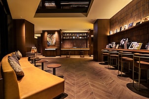 Ein stilvoller Lounge-Bereich mit einer Couch, runden Tischen, einer Bar mit Hockern und einem Bücherregal.