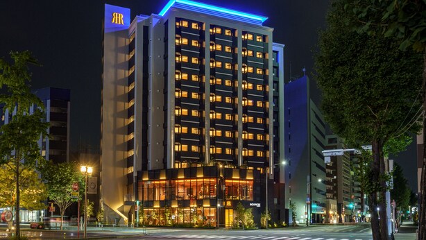 A multi-story hotel with a prominent 'JR' sign on the top left, a modern facade, and a well-lit entrance. - BOUNCEE by RIHGA Fukuoka Hakata (Fukuoka)