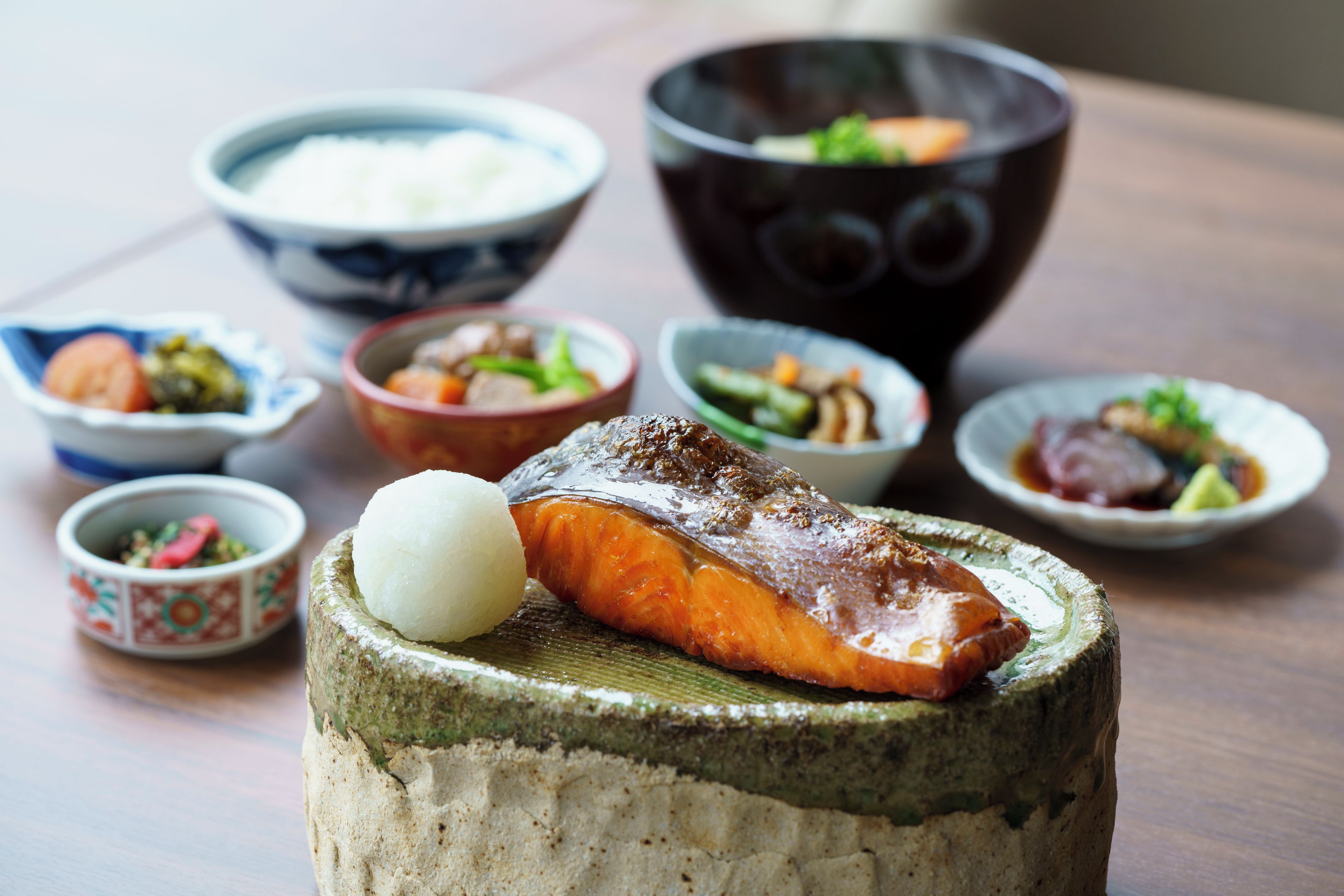 A variety of dishes including a salmon fillet on a wooden platter, surrounded by bowls of different foods.