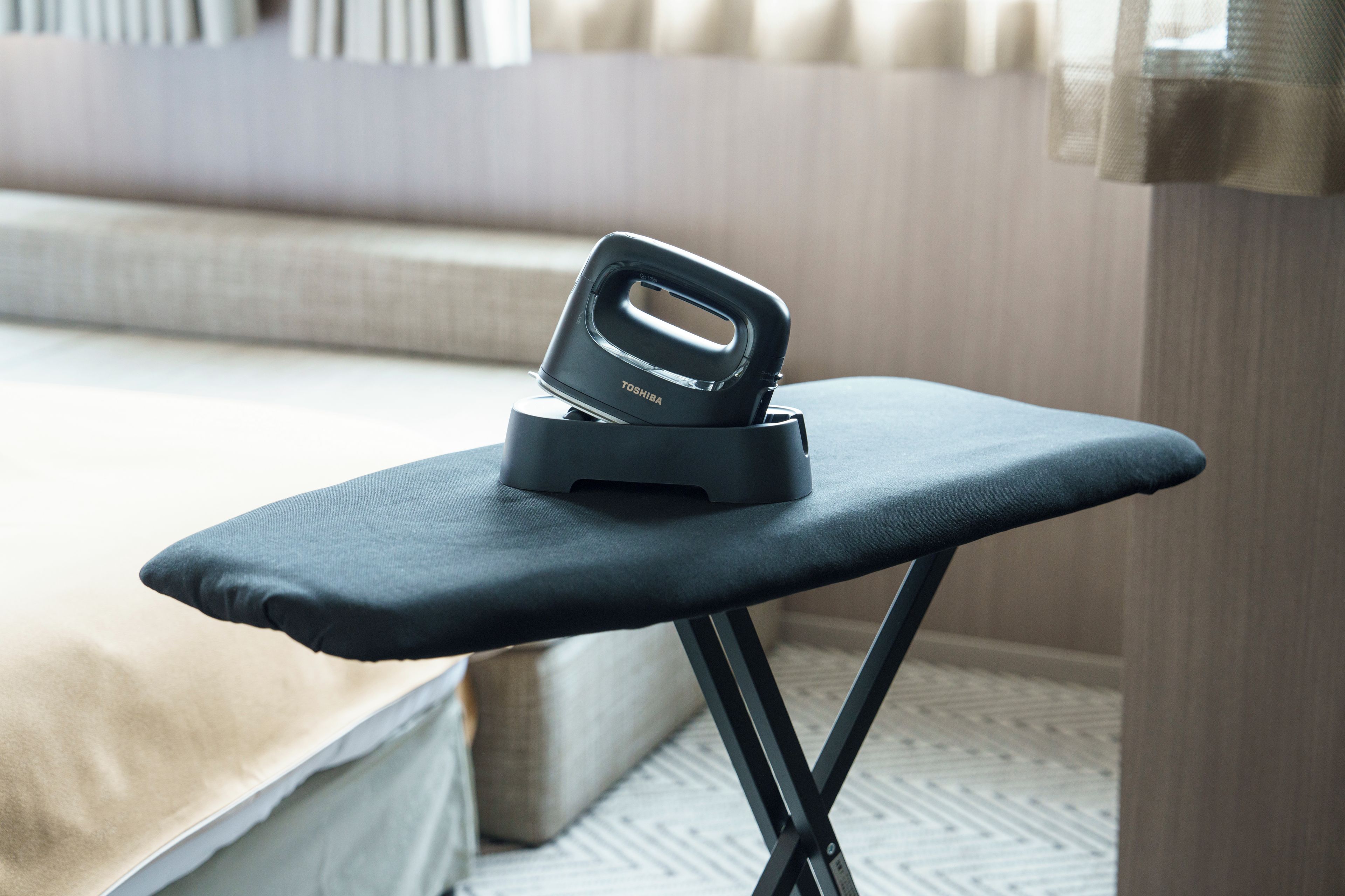 A black ironing board with a built-in iron on top, placed on a bed.