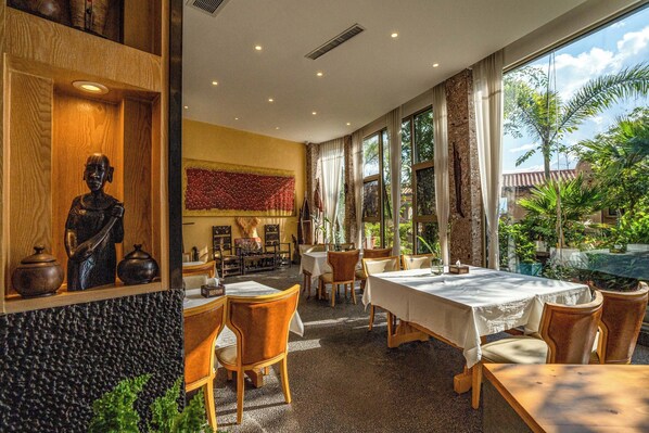 A restaurant with wooden furniture, a statue, and large windows overlooking a garden. - Dali Sea Coconut Muxin Yeelen Villa (Dali)