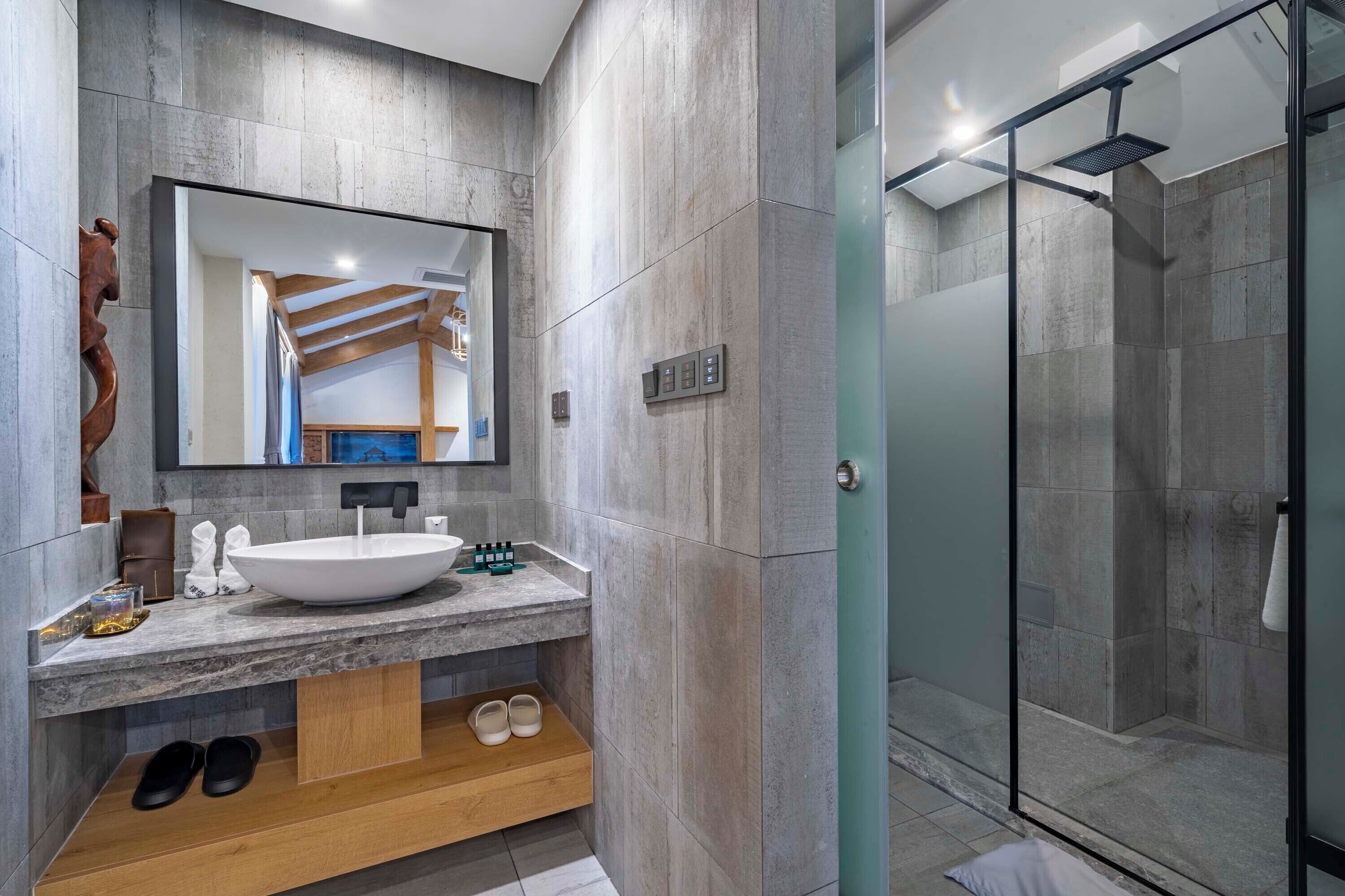 Une salle de bain moderne avec un grand miroir, un lavabo sur colonne et un espace douche.
