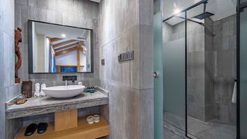 Une salle de bain moderne avec un grand miroir, un lavabo sur colonne et un espace douche.