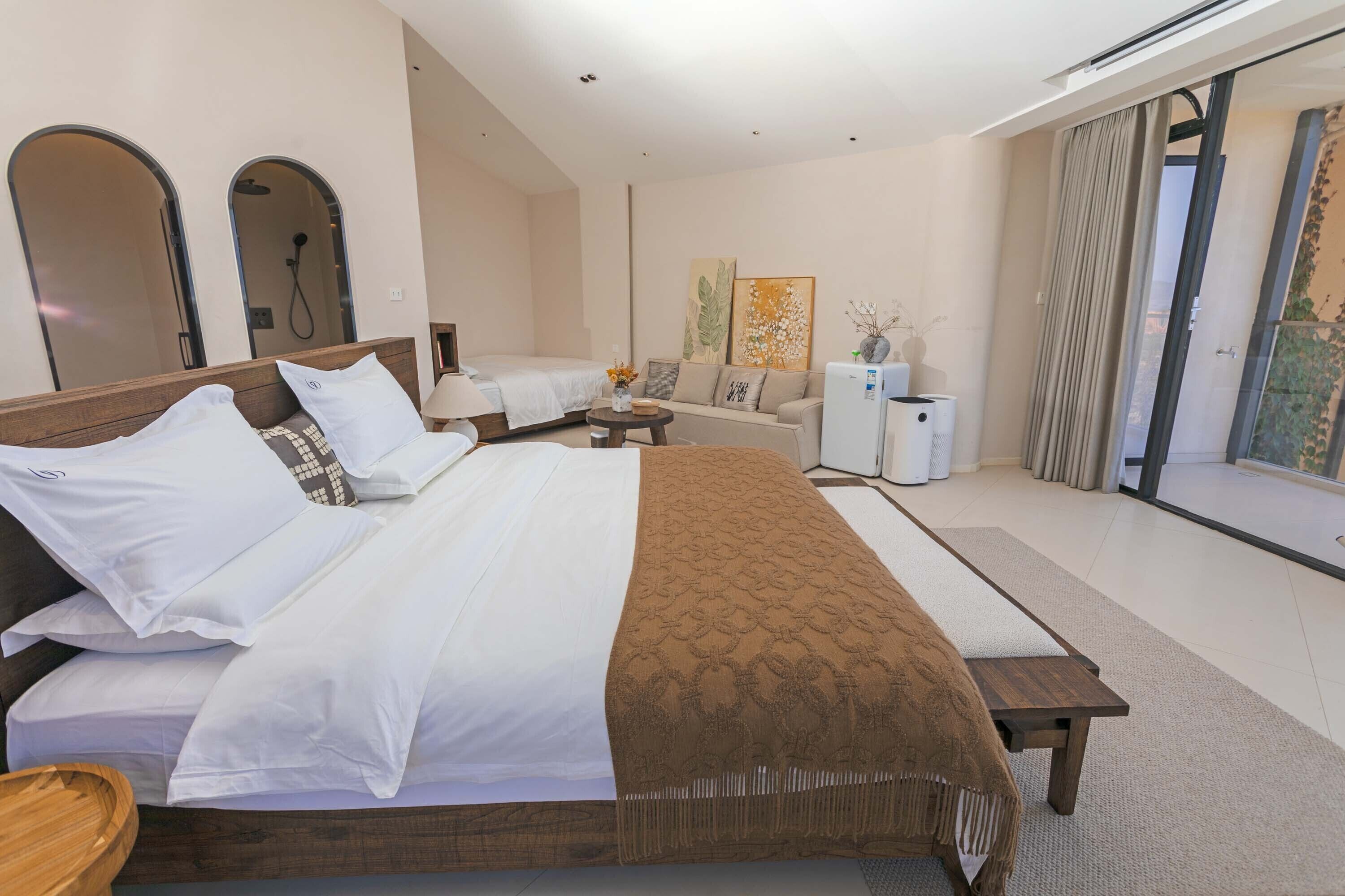 Une chambre d’hôtel moderne dotée d’un grand lit, d’un canapé, d’une petite table et offrant une vue sur l’extérieur grâce à une porte coulissante.