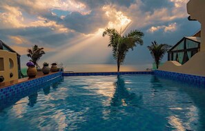 En swimmingpool med utsikt över havet, omgiven av palmer och en byggnad med modern design.
