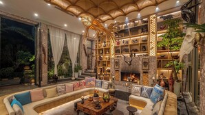 A luxurious living room with a curved sofa, a wooden coffee table, and a fireplace. There are shelves with decorative items and a large plant. - Dali Sea Coconut Muxin Yeelen Villa (Dali)