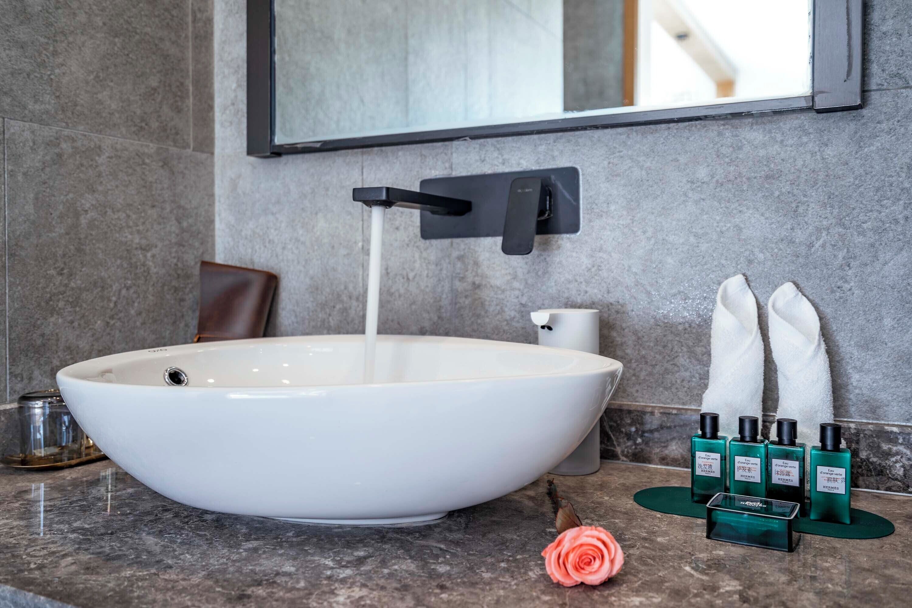 Een moderne badkamer met een grote witte wasbak, een zwarte kraan en een spiegel erboven.