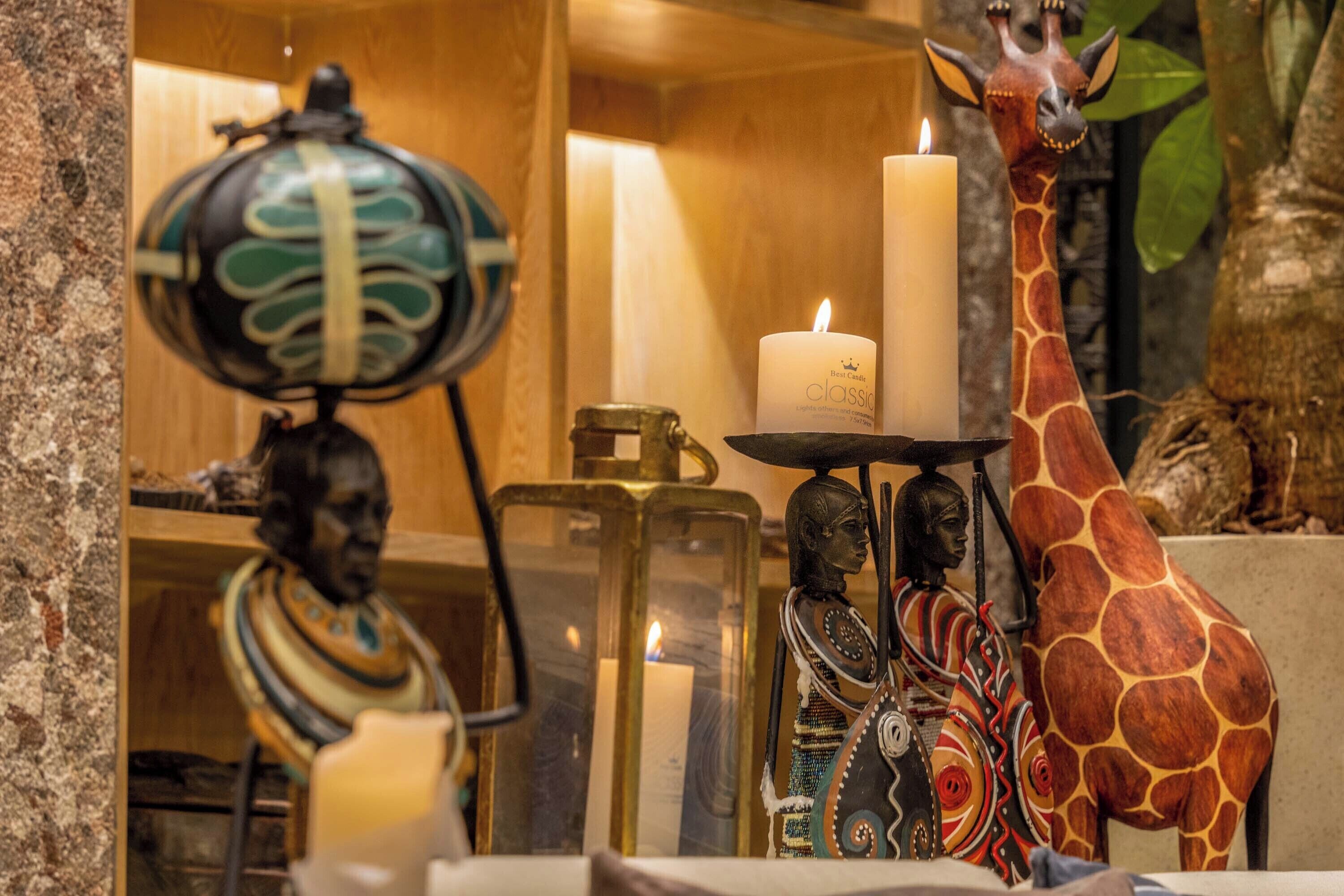 Una habitación con estante de madera que muestra varios objetos decorativos, incluyendo una estatua de jirafa, una lámpara y una vela.