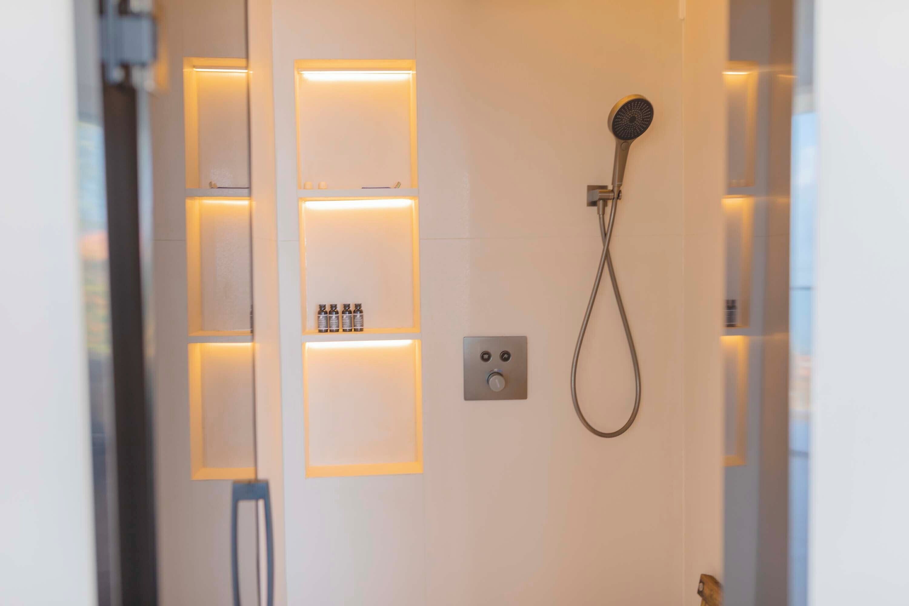 Een moderne badkamer met een douche, verlichte planken en een bedieningspaneel.