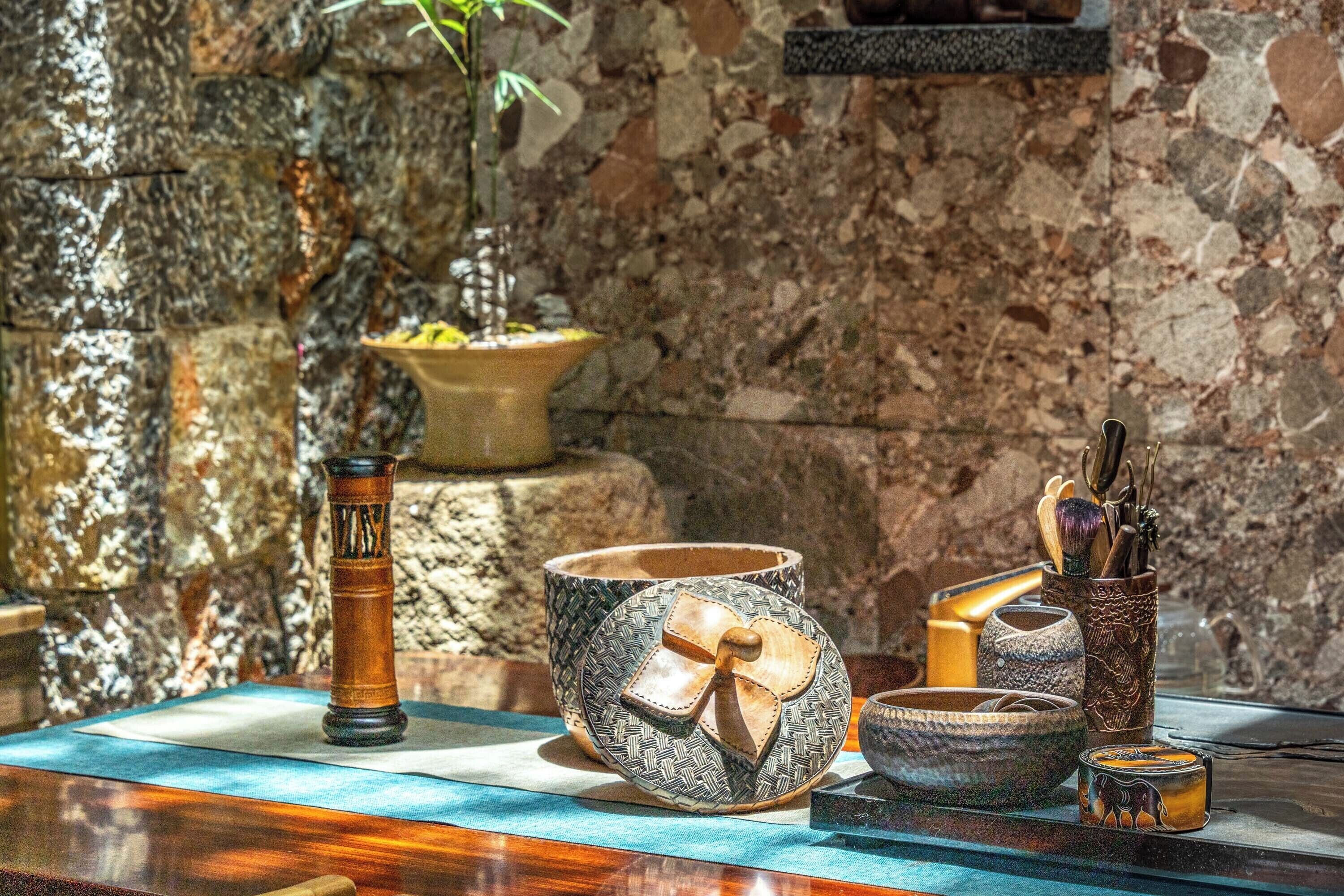 A stone wall, a potted plant, and various ceramic and metal objects on a table.