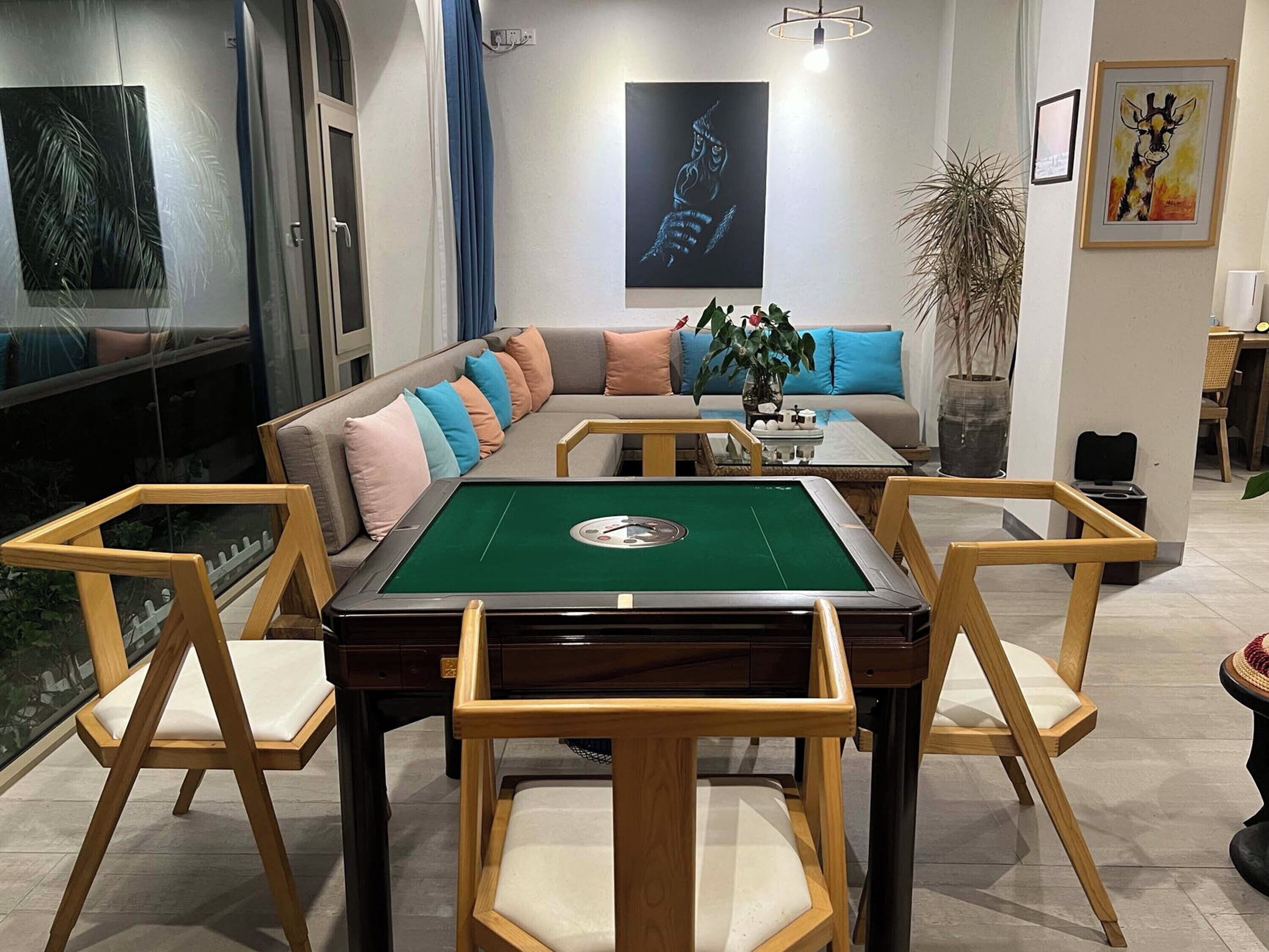 A pool table with wooden chairs, a sofa with colorful cushions, and artwork on the walls.