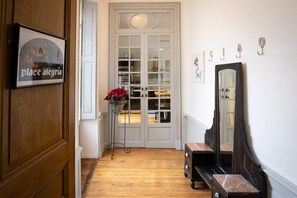 Un couloir avec un plancher en bois, une porte blanche, un miroir et un panneau encadré.