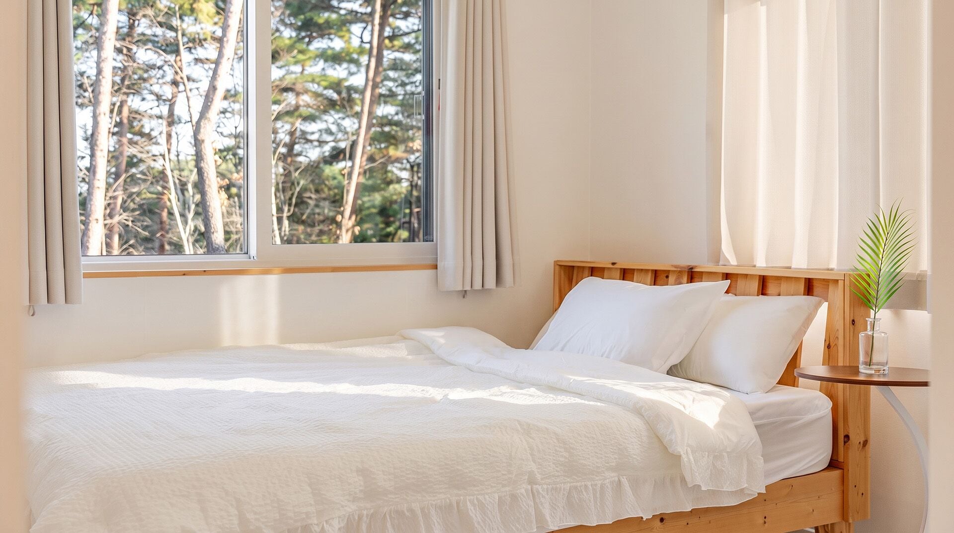 Una cama individual con cabecera de madera, ropa de cama blanca y una ventana con cortinas.