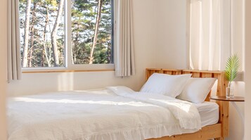 Una cama individual con cabecera de madera, ropa de cama blanca y una ventana con cortinas.