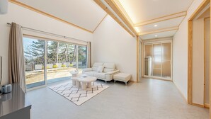 Un salon moderne avec un canapé, une table basse et une vue sur un jardin grâce à de grandes fenêtres.