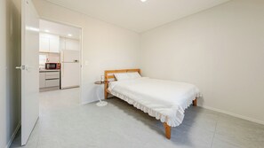 A bedroom with a single bed, a small bedside table, and a nightstand. There is a door leading to a kitchenette with a microwave and a refrigerator. - Gangneung Eondeokwie Pension (Gangneung)