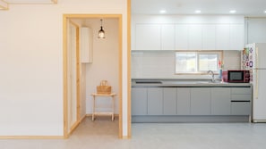 A modern kitchen with white cabinets, a microwave, and a window. - Gangneung Eondeokwie Pension (Gangneung)