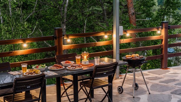 An outdoor dining area with a table set for a meal, a grill, and string lights. - Gangneung Eondeokwie Pension (Gangneung)