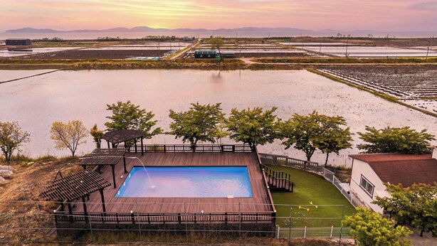 A swimming pool with a wooden deck, surrounded by trees and a view of a large body of water. - Ganghwa Aboha Pet-friendly Pension (Incheon)