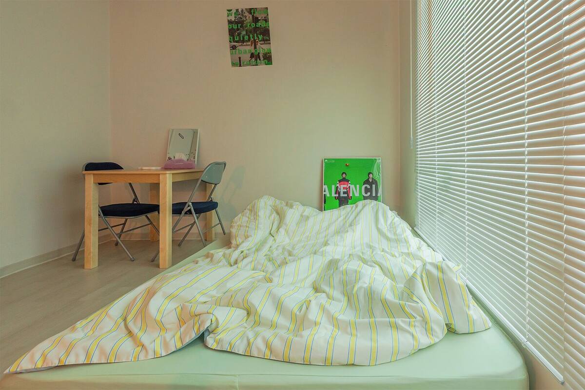 Una habitación con cama, escritorio, silla y ventana con persianas.