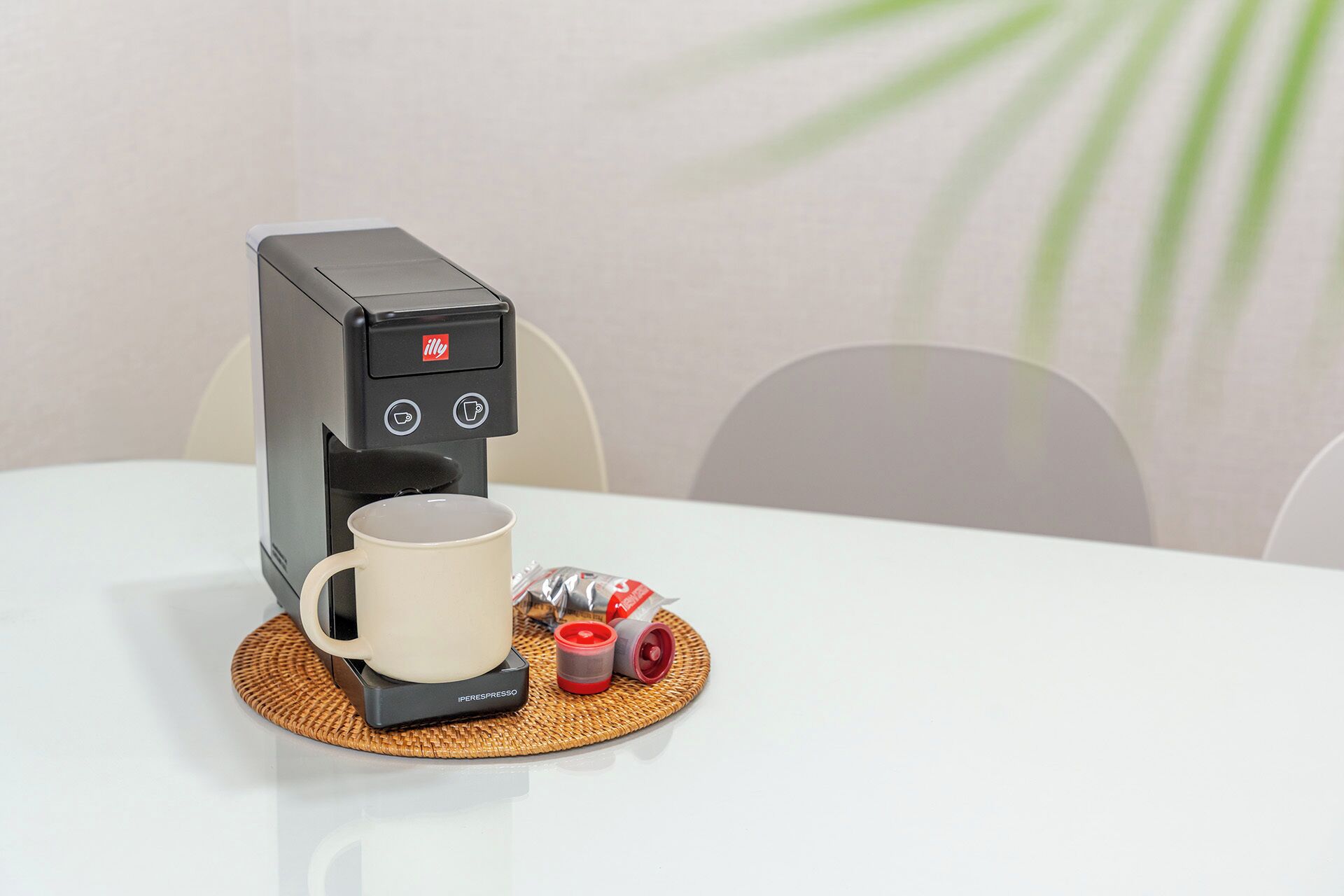 A coffee machine on a table with a white mug and a coffee pod.