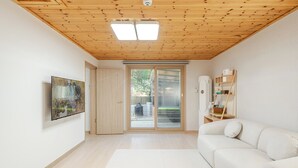 Una habitación con techo de madera, puerta corredera de vidrio que da a un espacio exterior, un sofá blanco y un televisor montado en la pared.