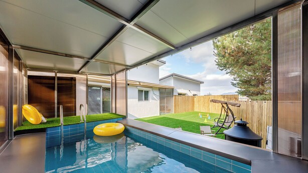 Una piscina con tobogán, un flotador inflable pequeño y una cerca de madera en un patio trasero.