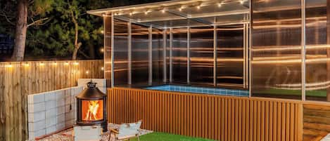 A covered outdoor area with a fire pit, seating, and a pool.