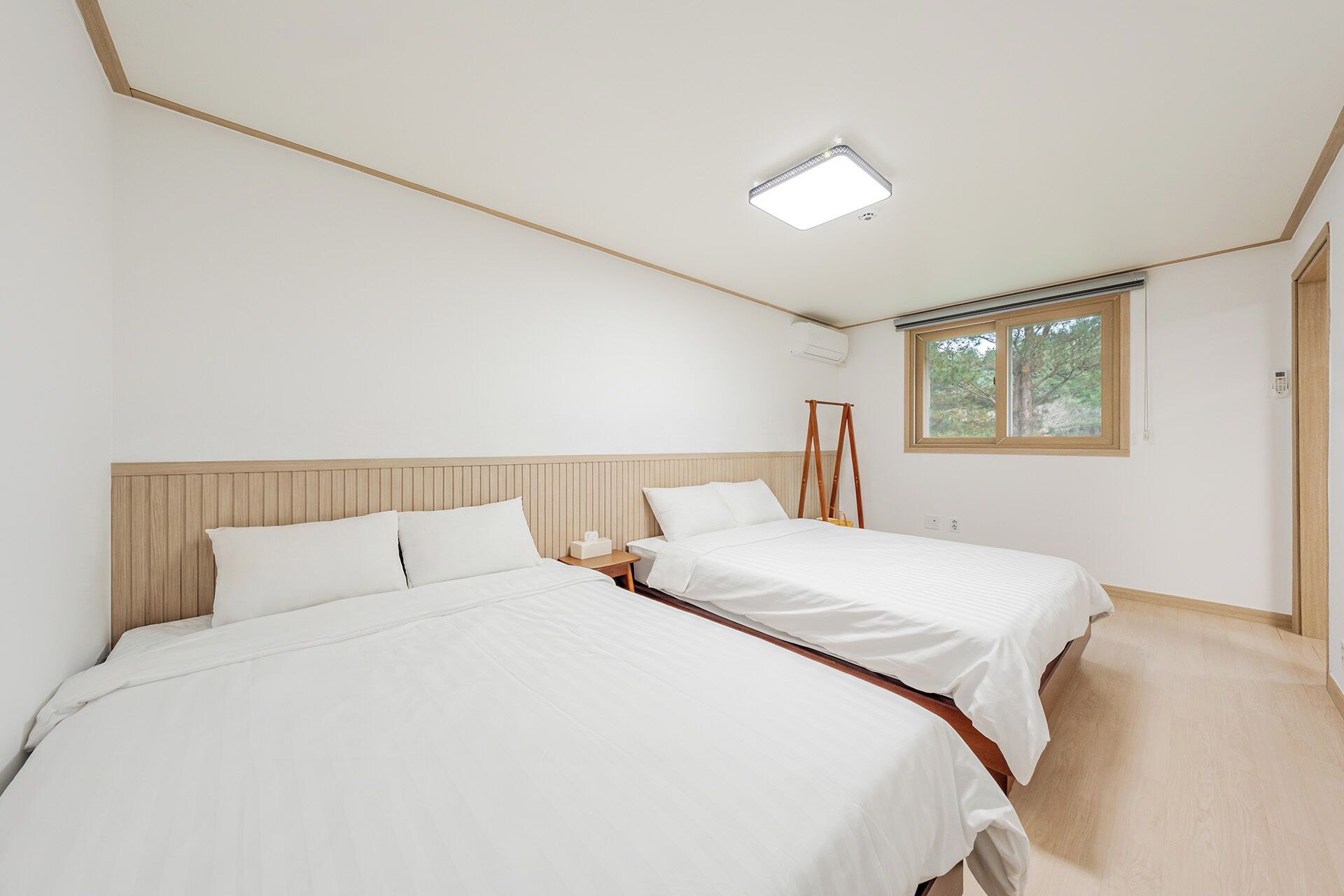 Une chambre avec deux lits, un luminaire au plafond, une fenêtre et une échelle en bois.