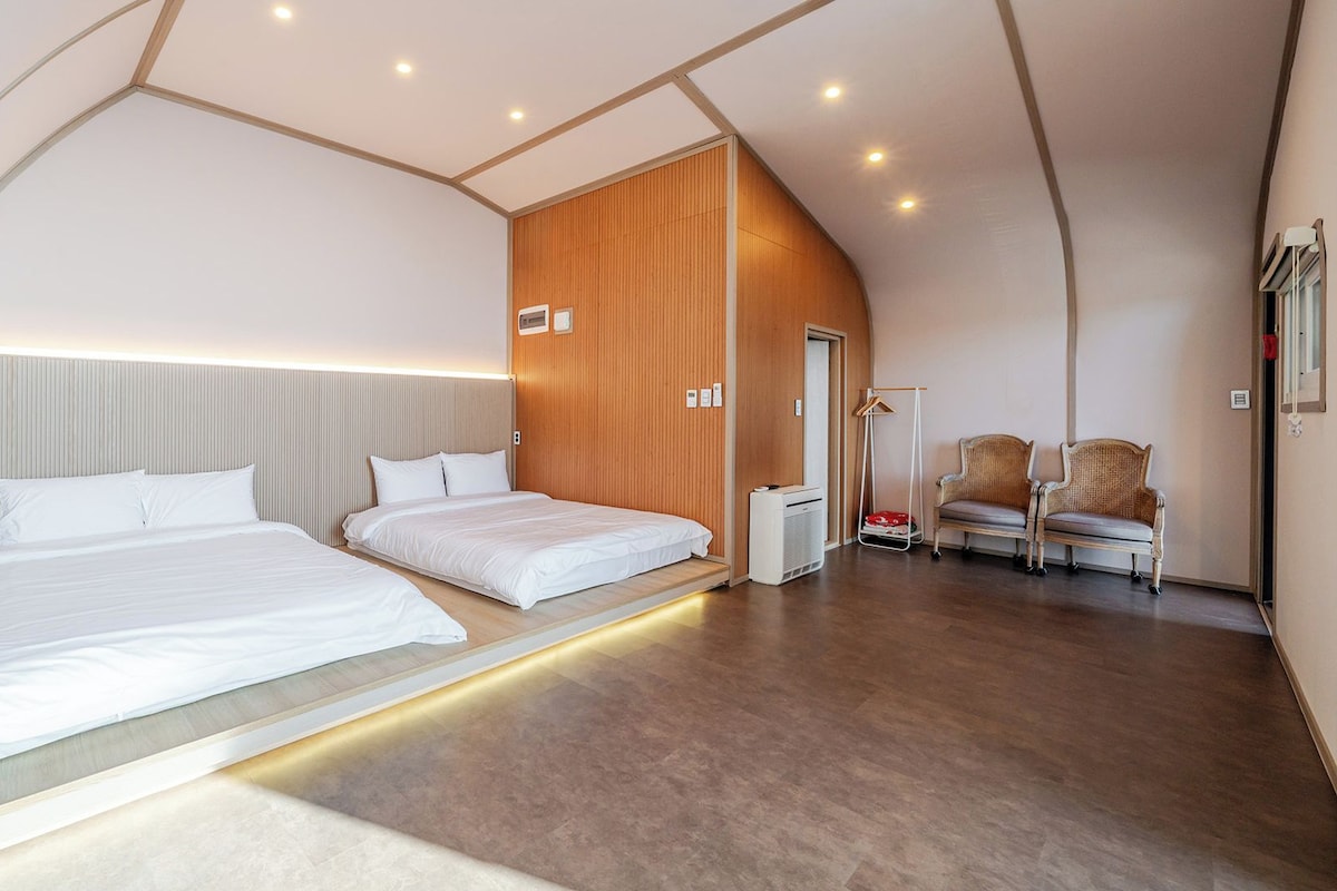 A modern hotel room with a large bed, bedside tables, a wardrobe, a seating area with chairs, and a walk-in closet.