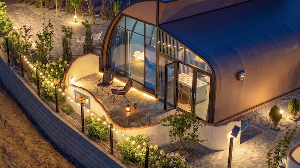 Une maison moderne dotée d’une façade en verre incurvée, d’un espace extérieur aménagé pour se détendre et d’un jardin bien éclairé.