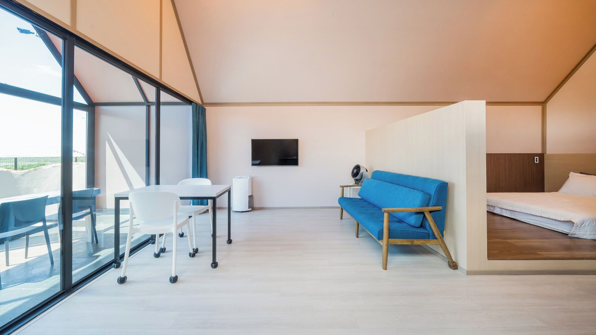 A modern hotel room with a large window, a desk, a blue sofa, and a bed.
