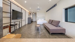A modern hotel room with a sofa, a bed, a TV, a small kitchen area, and a large window. - Sokcho W Spa Poolvilla (Sokcho)