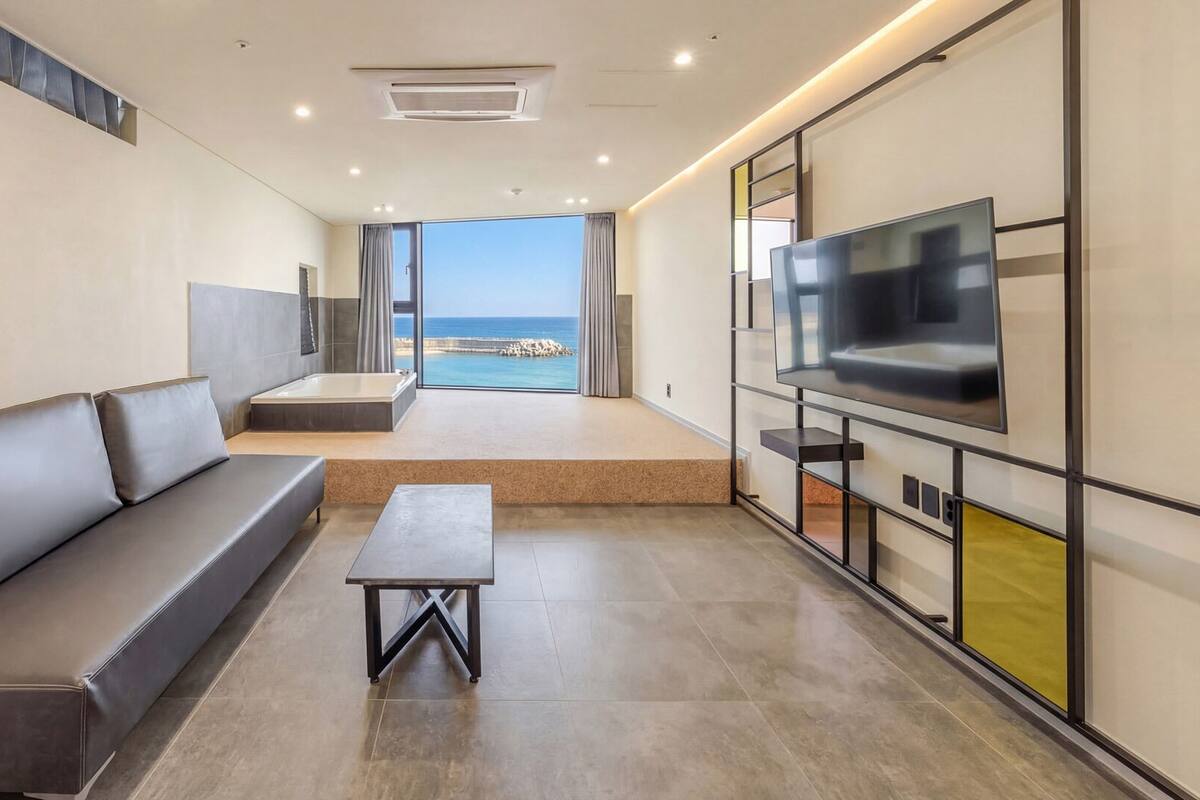 A modern living room with a sofa, a coffee table, a TV, and a view of the sea.