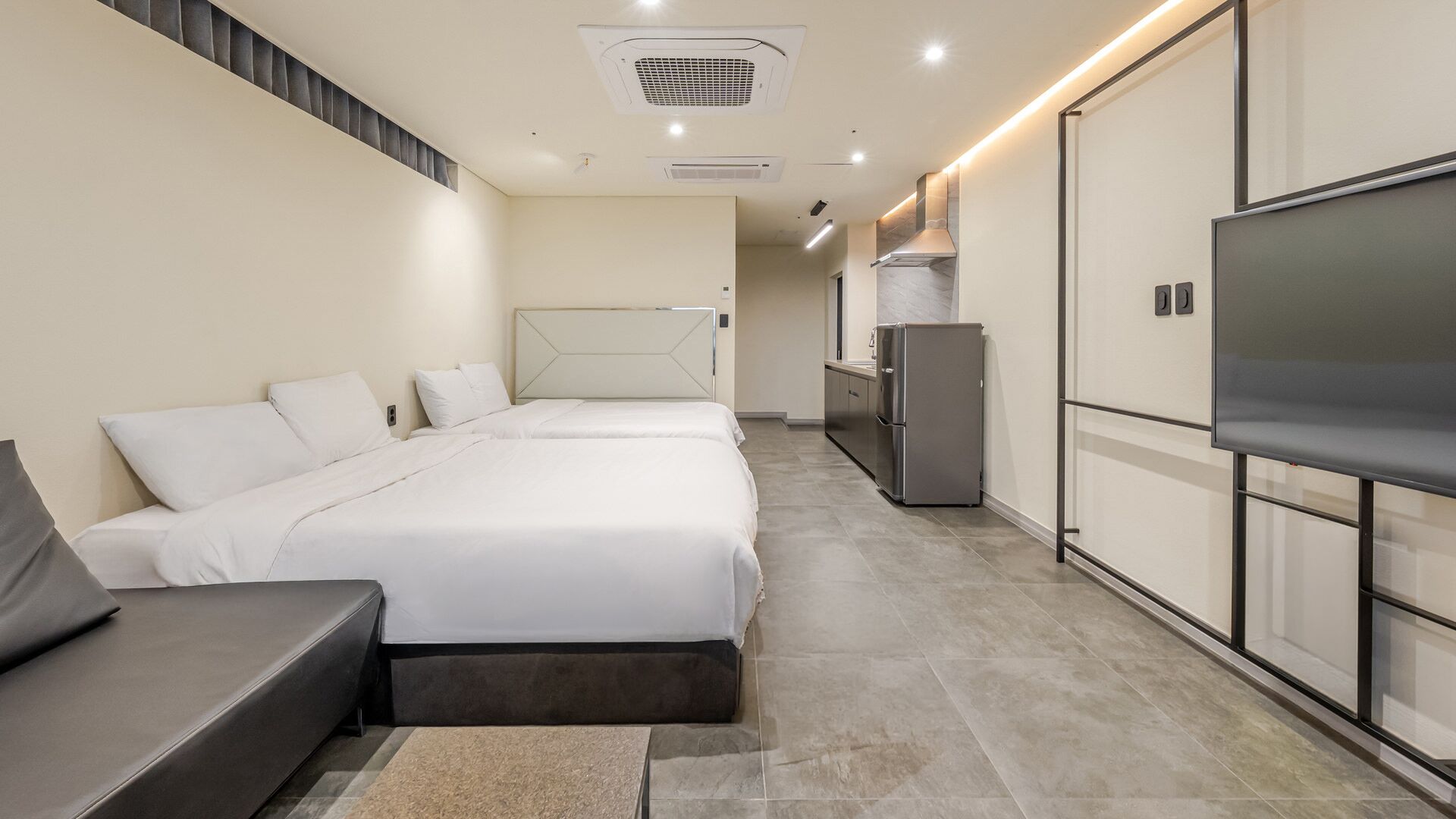 A modern hotel room with a bed, a sofa, a TV, and a kitchenette.