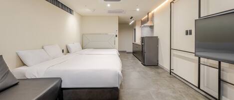 A modern hotel room with a bed, a sofa, a TV, and a kitchenette.